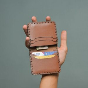 A hand holding a leather wallet containing various cards and cash.